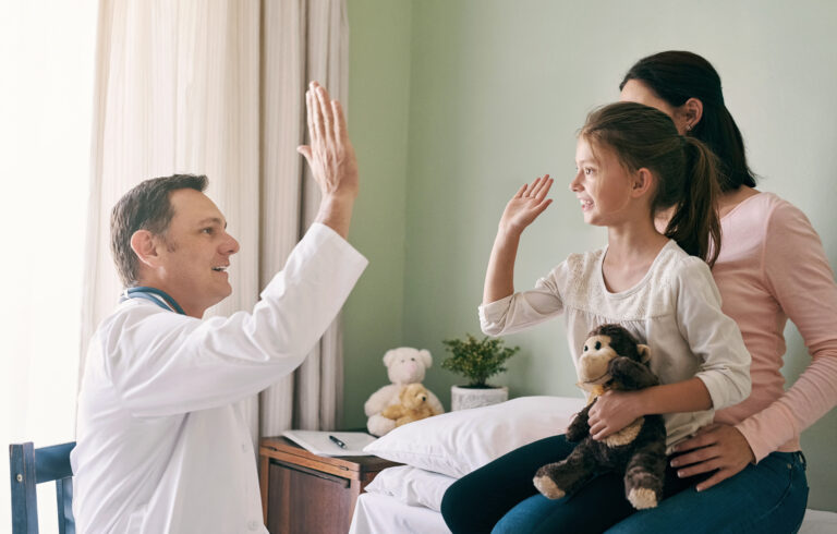 Doctor high-fiving girl with teddy bear.